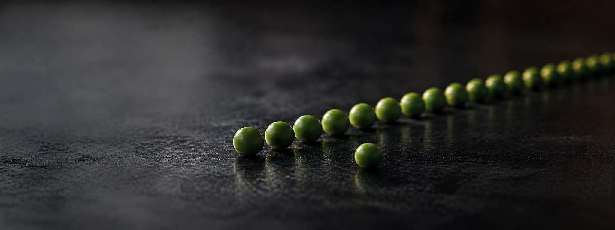 A row of green peas on dark slate, with one pea set apart.